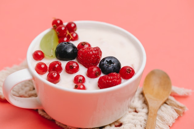 cup of yogurt with fruit in it and on a pink background with a wooden spoon laying next to the cup